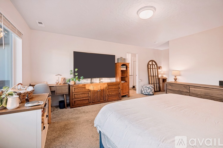 A bedroom with a large bed, a desk with a chair, a dresser, and a window with a view of the city.