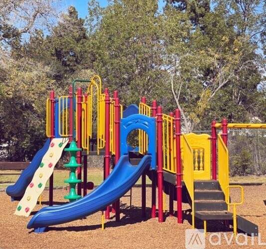 A playground with a blue and green slide, a yellow and red climbing frame, and a yellow staircase.