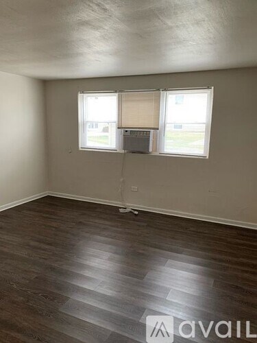 A room with wooden flooring and two windows.