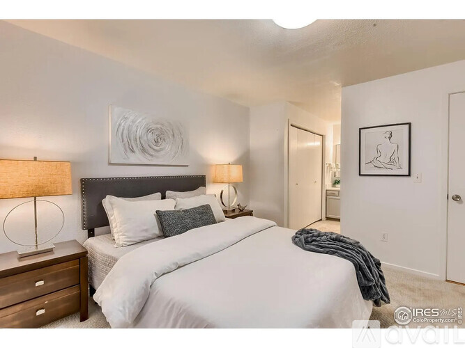 A bedroom with a large bed, a nightstand with a lamp, and a framed picture on the wall.