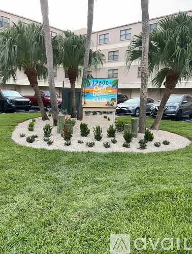 A sign for a club is surrounded by palm trees and small bushes.