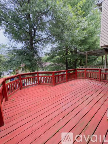 A red wooden deck with a railing and trees in the background.
