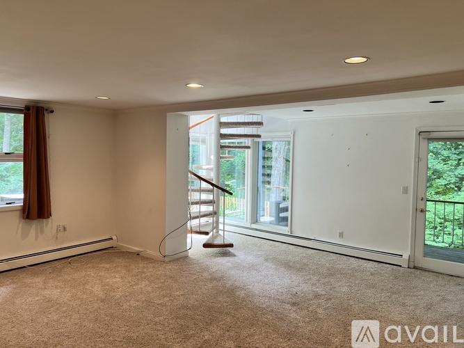 A spacious room with a carpeted floor, a staircase, and a view of the outdoors through a glass door.
