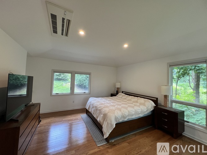 A bedroom with a large bed, a television, and a window overlooking a green area.