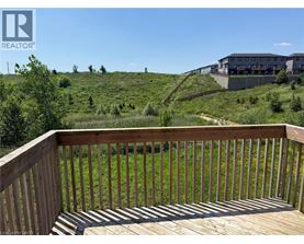 A wooden deck overlooks a grassy hill with a building in the distance.