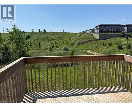 A wooden deck overlooks a grassy hill with a building in the distance.