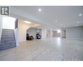A spacious room with wooden flooring and a staircase on the left side.