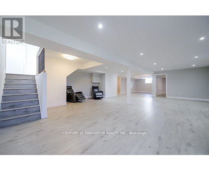A spacious room with wooden flooring and a staircase on the left side.