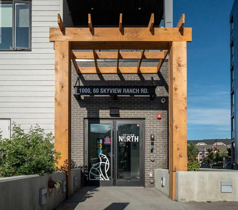 The image shows the front of a building with a wooden structure above the entrance and a glass door with a bicycle symbol on it.
