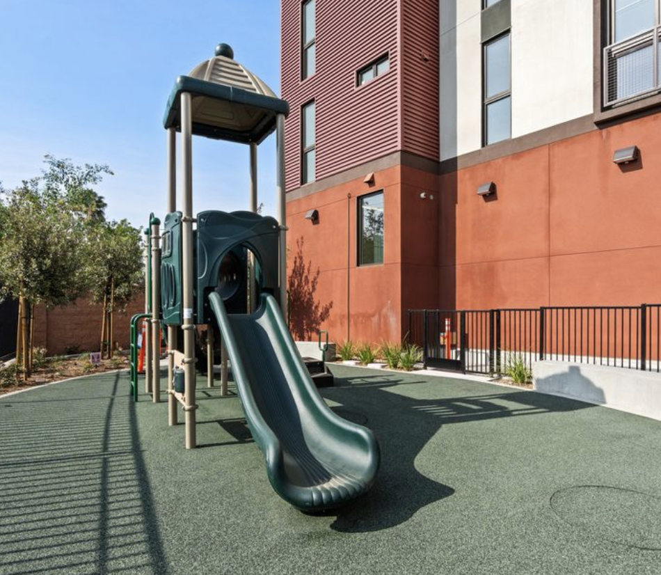 A playground with a green slide and a wooden structure.