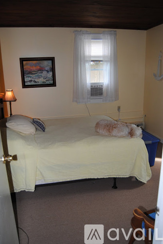 A bedroom with a bed, a lamp, a window with a curtain, and a painting on the wall.