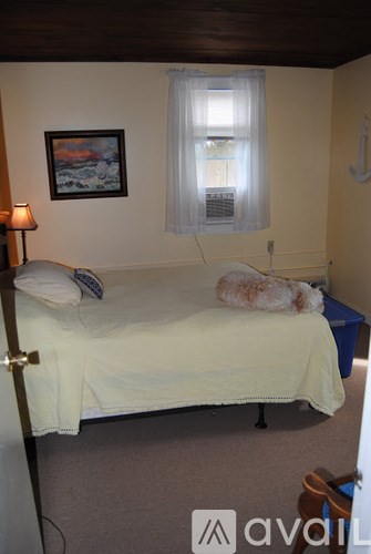 A bedroom with a bed, a lamp, a window with a curtain, and a painting on the wall.