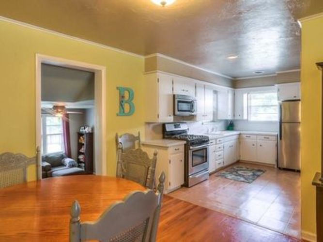 A kitchen with a wooden table and chairs in the foreground and a white fridge in the background.