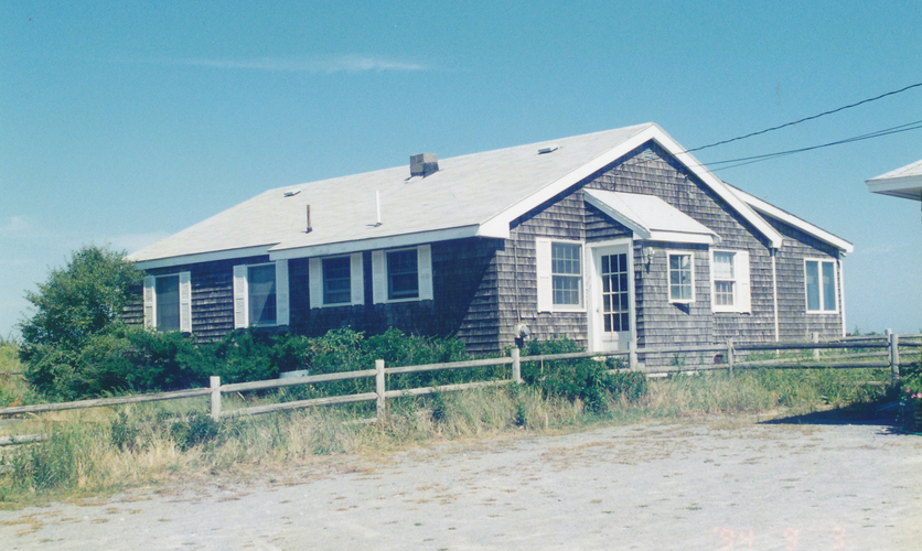 A house with a grey roof and white trim is surrounded by a white fence.