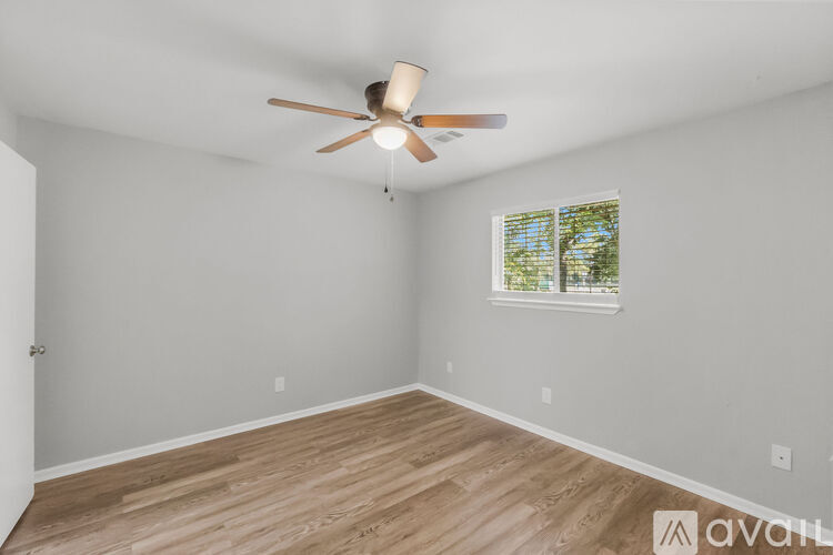 A room with a ceiling fan and a window with a view of trees.
