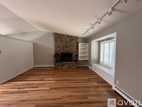 A spacious room with wooden flooring and a stone fireplace.