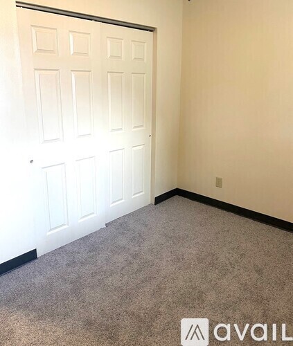 A carpeted room with a white door and a wall with a light switch.