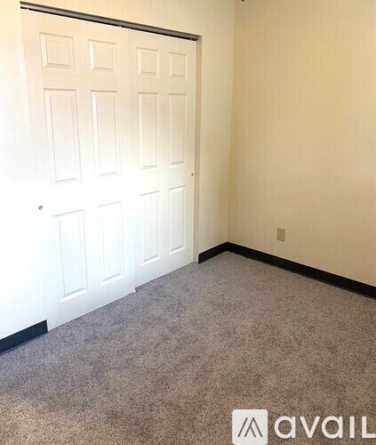 A carpeted room with a white door and a wall with a light switch.