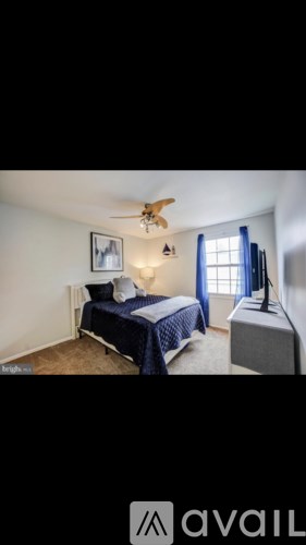 A bedroom with a bed, a ceiling fan, and a window with blue curtains.