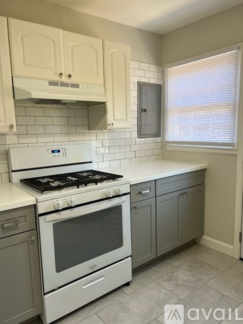 A kitchen with a white stove and grey cabinets.