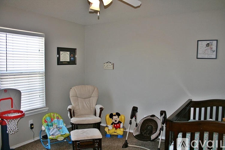 A baby room with a rocking chair, a baby swing, a fan, a crib and a Mickey Mouse.