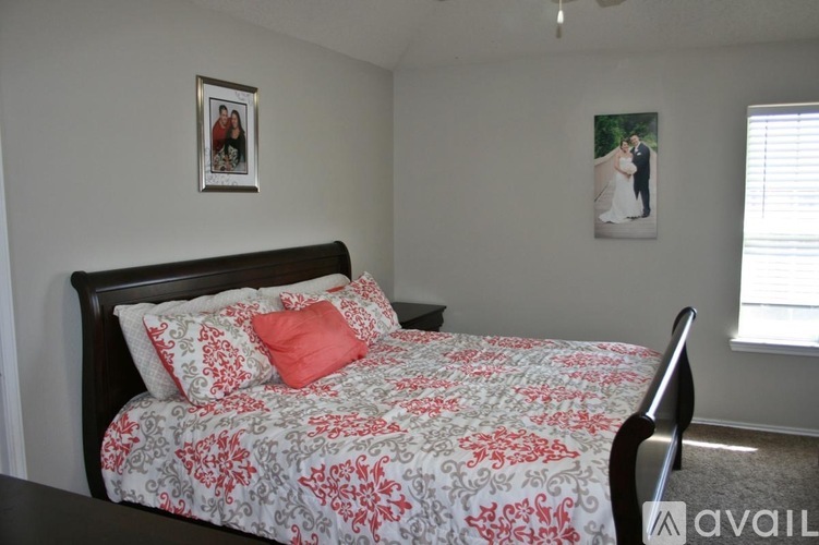 A bed with a red and white comforter is in the foreground of a bedroom with a framed picture of a couple on the wall.