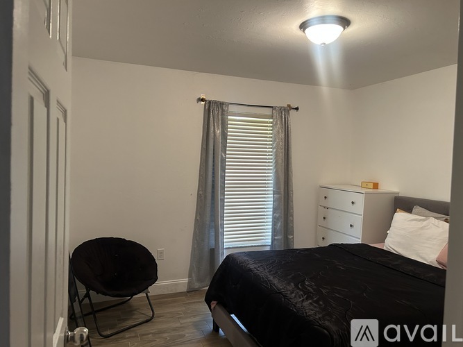 A bedroom with a black bed, a chair, and a nightstand with a lamp.