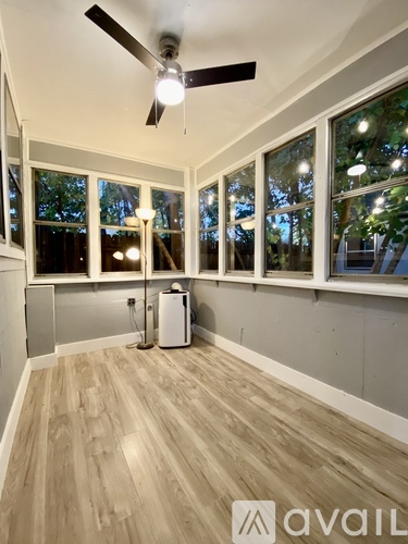 A room with a ceiling fan and a window with a view of trees.