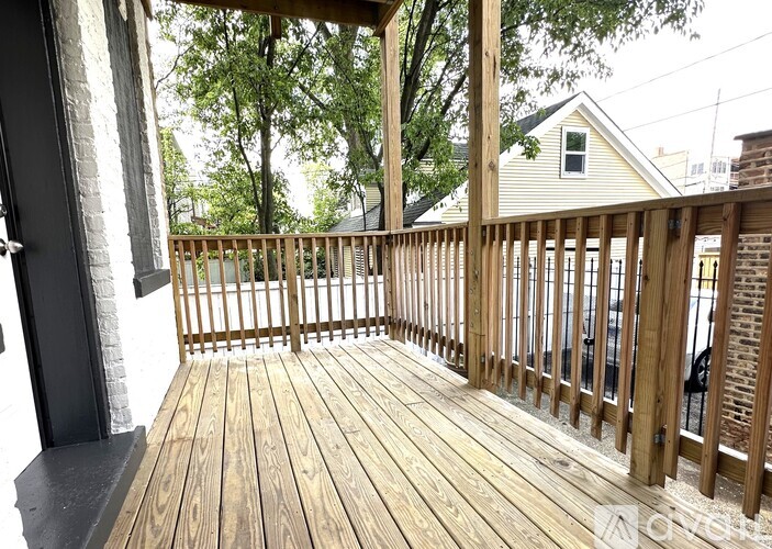 A wooden deck with a railing and a view of a house and trees.