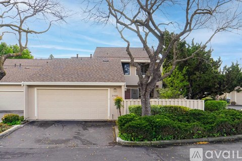A house with a brown roof and a garage door is surrounded by trees and bushes.