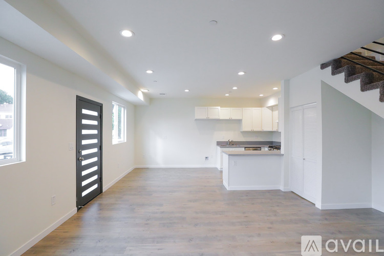 A spacious, empty room with wooden floors and a staircase on the right side.