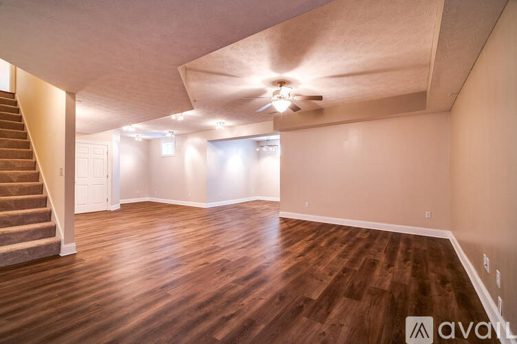 A spacious room with wooden flooring and a staircase on the left side.