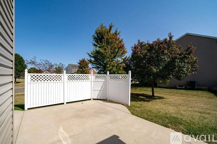 A white fence with lattice work divides a driveway from a grassy area.