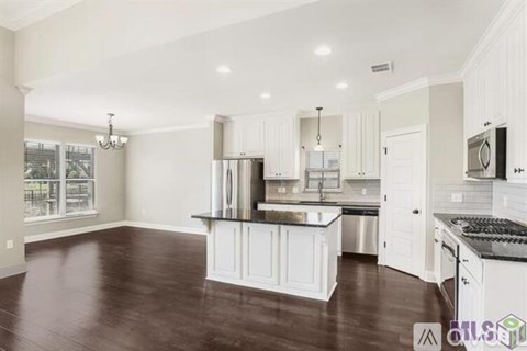 A spacious kitchen with white cabinets and a dark wood floor.