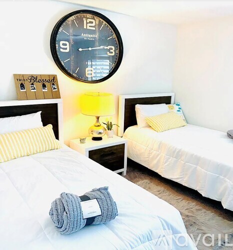 A bedroom with two beds, a nightstand with a lamp, and a clock on the wall.