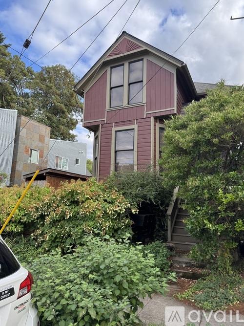 A house with a red and white exterior is surrounded by greenery and a car is parked in front.