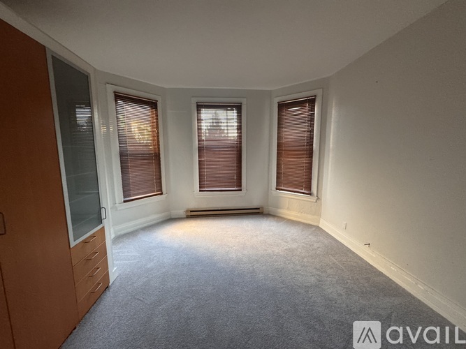 A room with carpeted floor, two windows with blinds, and a wooden door.