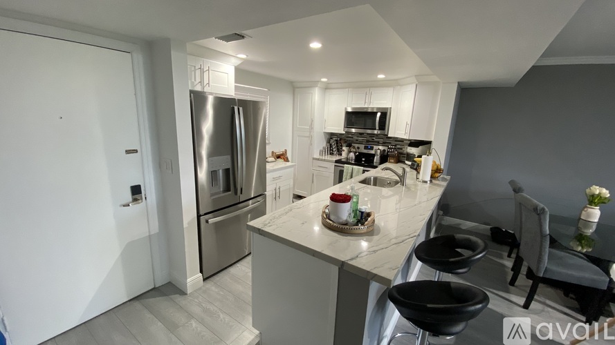 A modern kitchen with a stainless steel refrigerator and black bar stools.