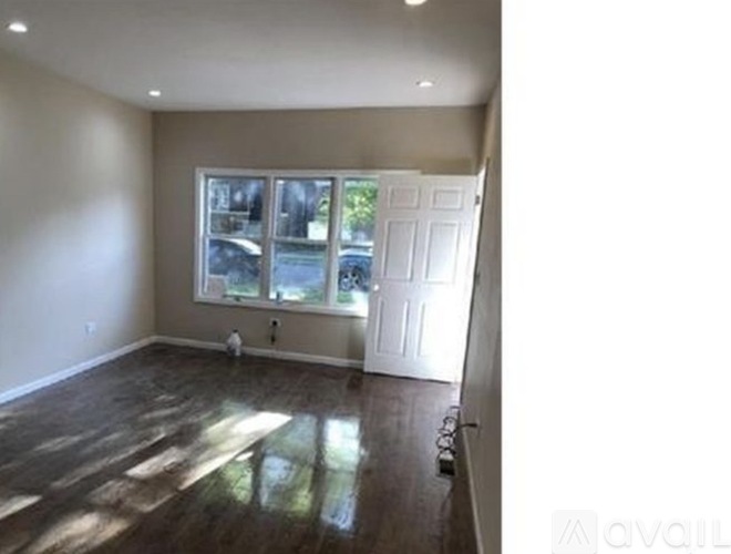 A room with wooden floors and a window showing a view of trees and a car.