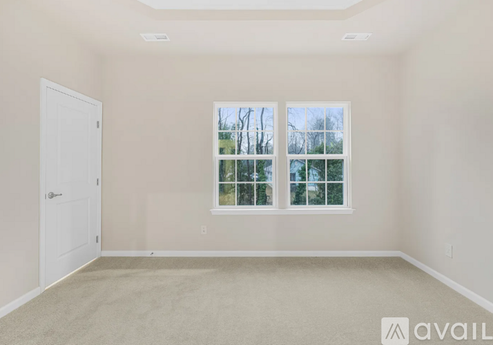 A room with a carpeted floor, a window with a view of trees, and a door.