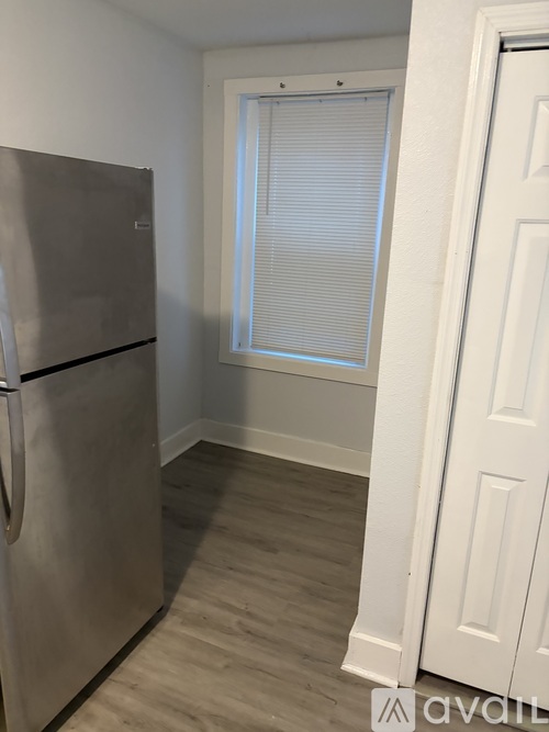 A kitchen with a stainless steel refrigerator and a window with blinds.