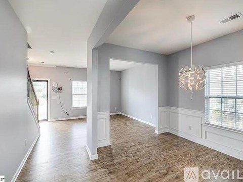 A spacious room with wooden flooring and a chandelier hanging from the ceiling.