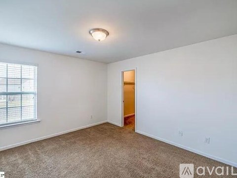 A room with a carpeted floor, a window with blinds, and a door leading to another room.