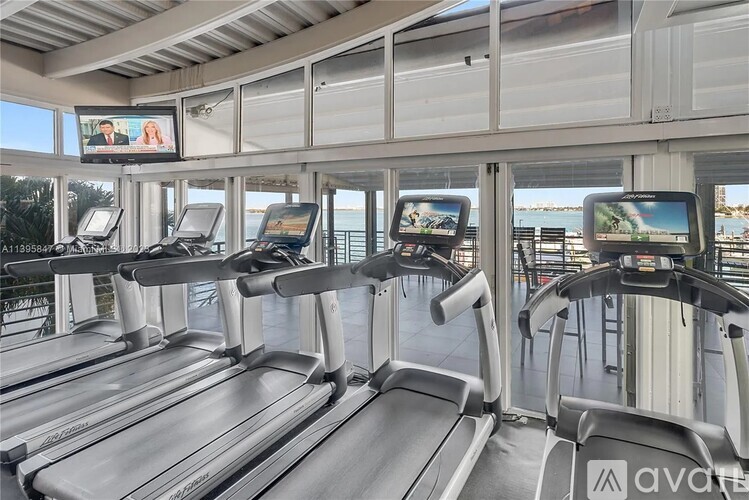A row of treadmills in a gym with a view of the outside.