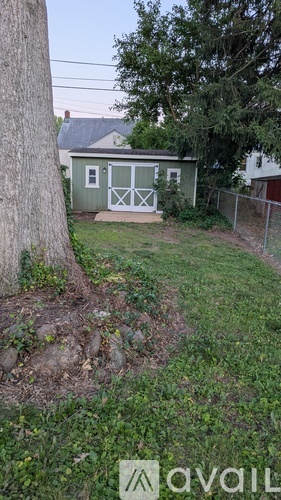A green shed with a white door is surrounded by a grassy area and a tree.