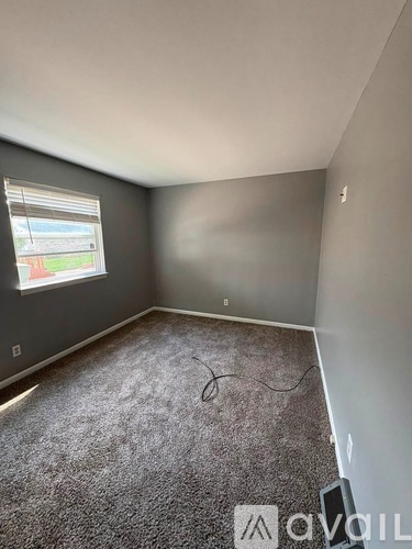 A room with grey carpet and a window showing a view of a street.