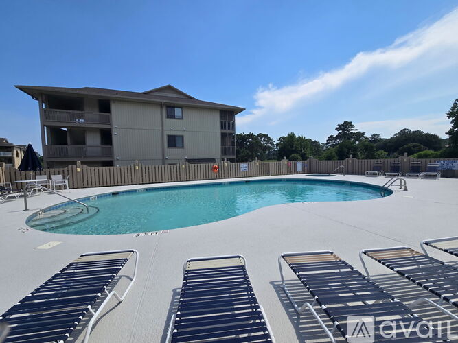 A pool with sun loungers and a building in the background.