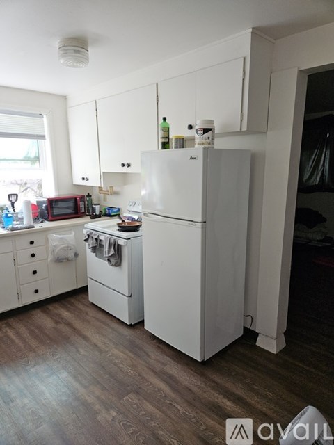 A white refrigerator stands in a kitchen with wooden floors and white cabinets.
