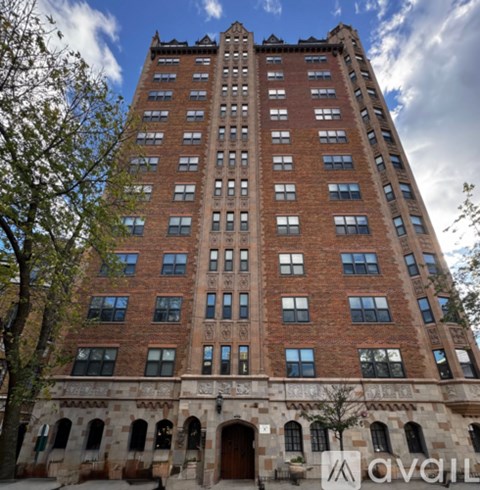 A tall red brick building with many windows and a stone archway at the base.