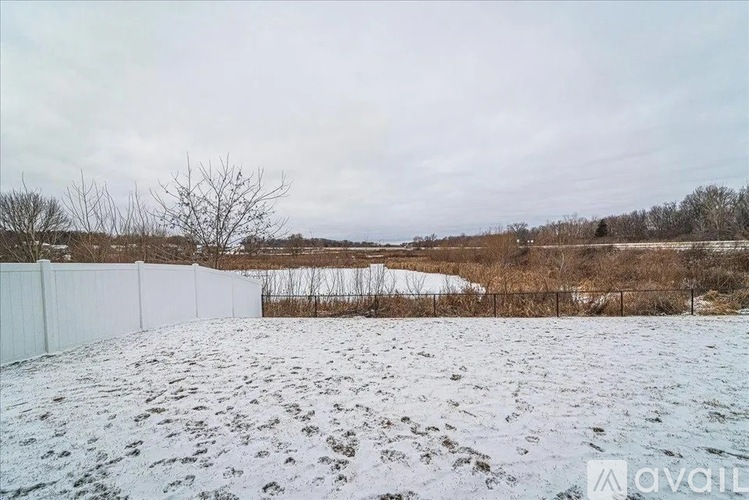A snow-covered field with a white fence in the foreground and bare trees in the distance.